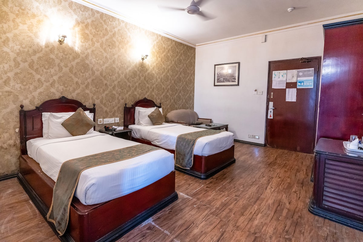 Ein Hotelzimmer mit zwei Betten, Holzboden, Deckenventilator und einer Tür mit einem Korkbrett.