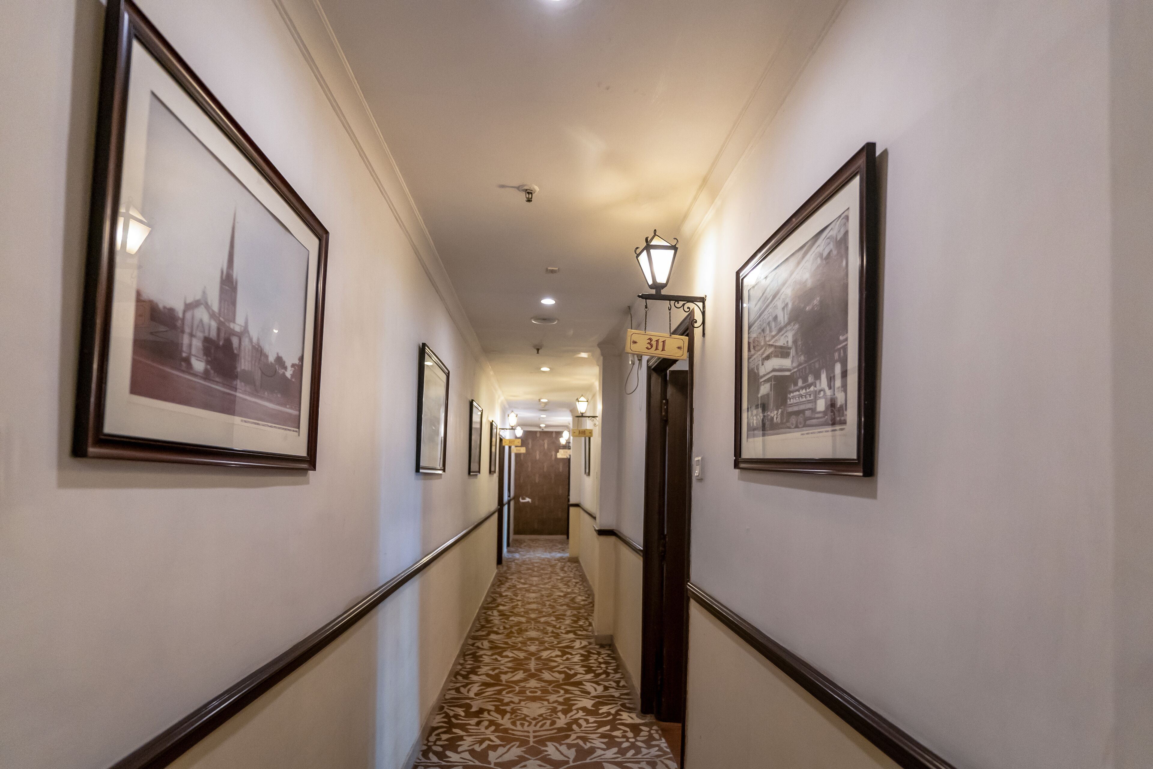 A hallway with framed pictures on the walls, a carpeted floor, and a sign indicating room number 311.