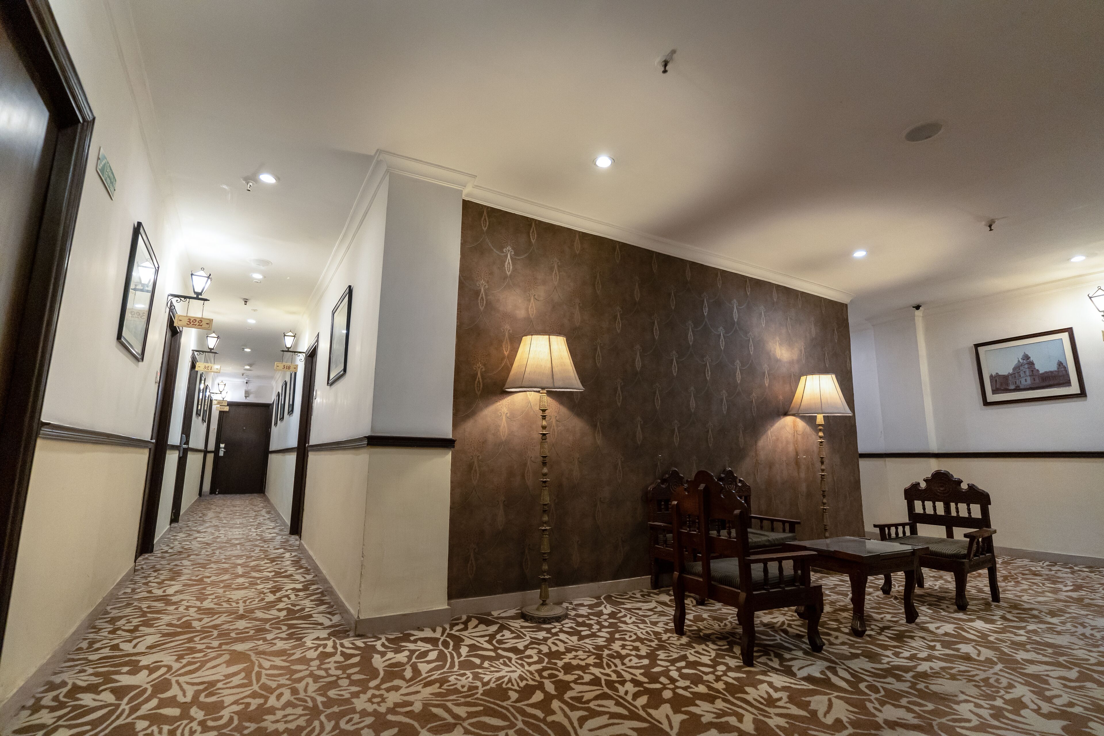 Un vestíbulo de hotel con alfombra estampada, un mostrador de recepción, dos lámparas fijadas a la pared y un cuadro enmarcado.