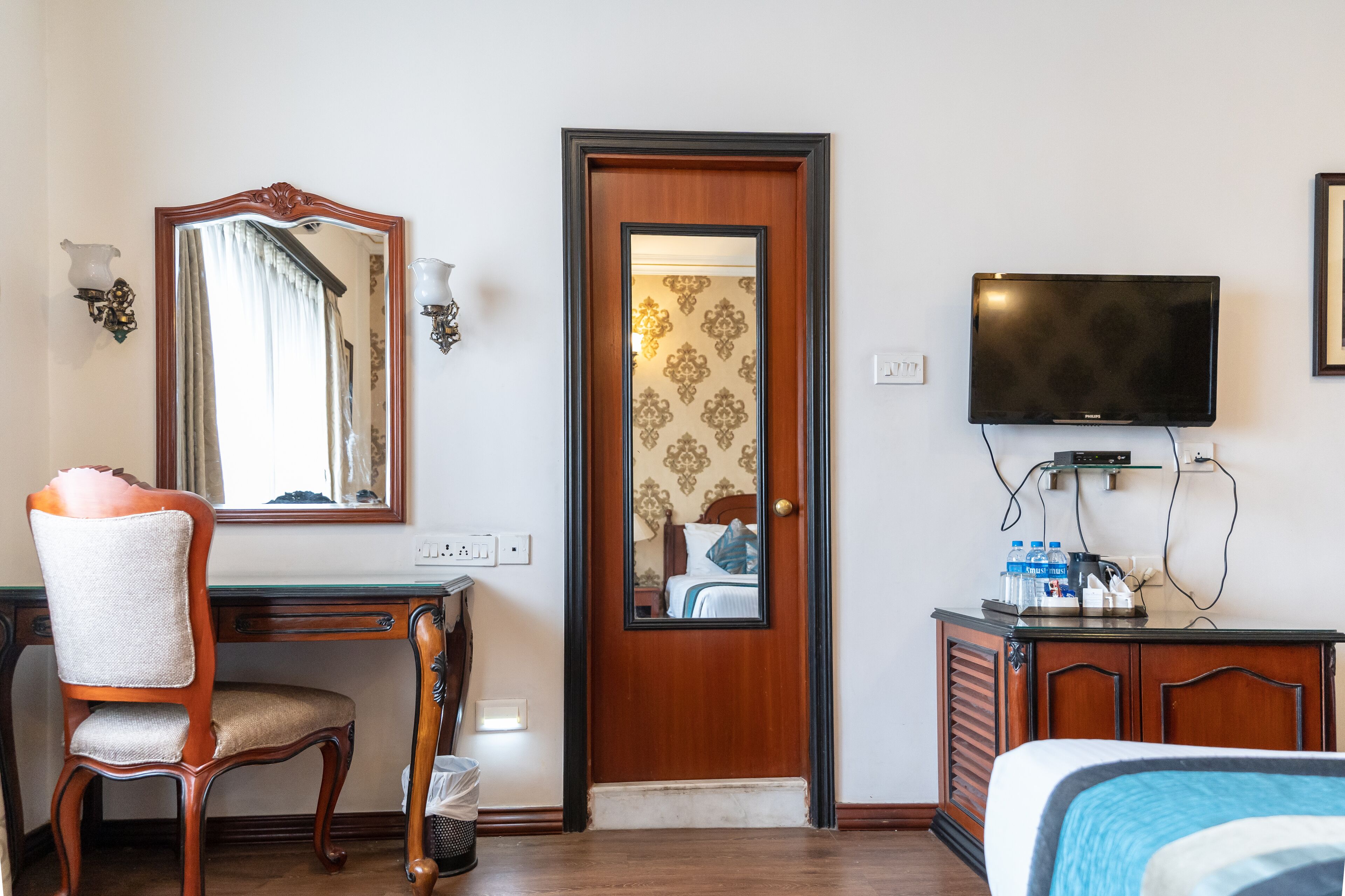 Une chambre d’hôtel avec un bureau en bois, une chaise, un lit, une télévision et une porte recouverte d’un papier peint à motifs.
