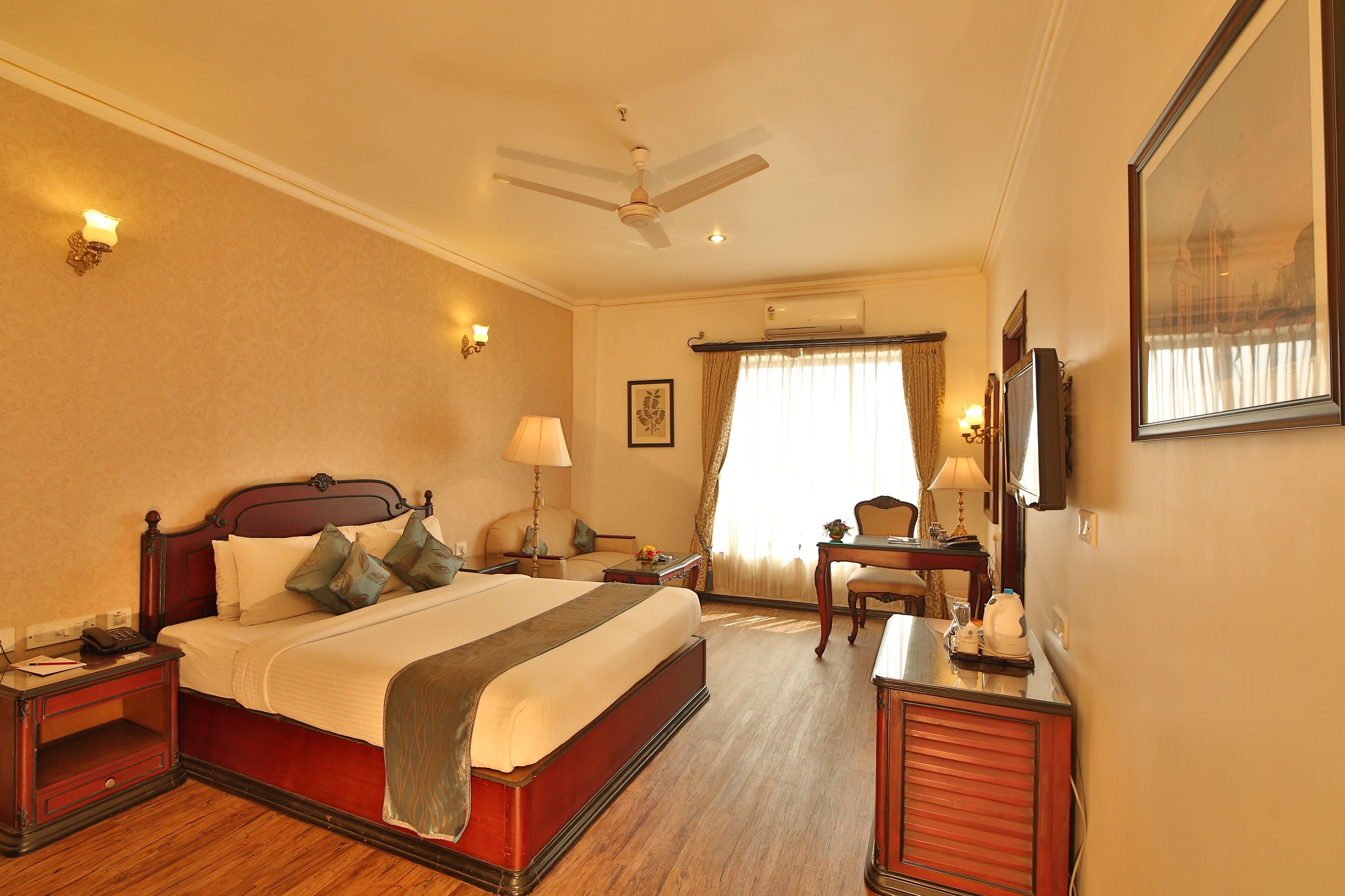 Une chambre d’hôtel avec un grand lit, des tables de chevet, un bureau, une chaise, un ventilateur de plafond et un grand miroir.
