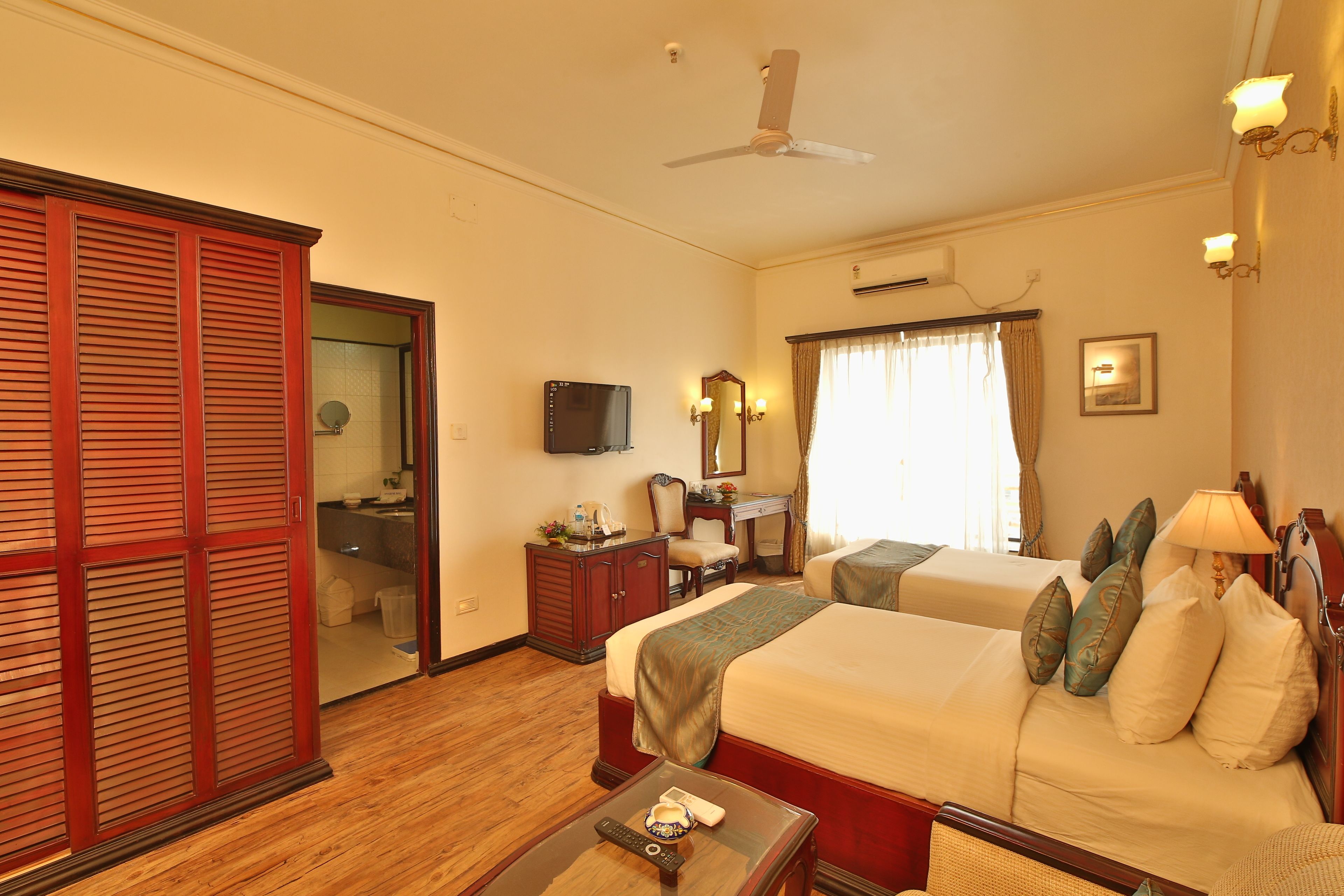 A hotel room with two beds, a desk, a mirror, and a wardrobe.