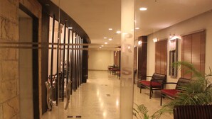 A hotel lobby with a marble floor, wooden chairs, and a potted plant. - The Lindsay (Kolkata)