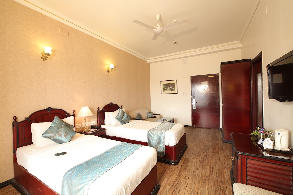 A hotel room with two beds, a desk with a telephone, and a television on the wall.