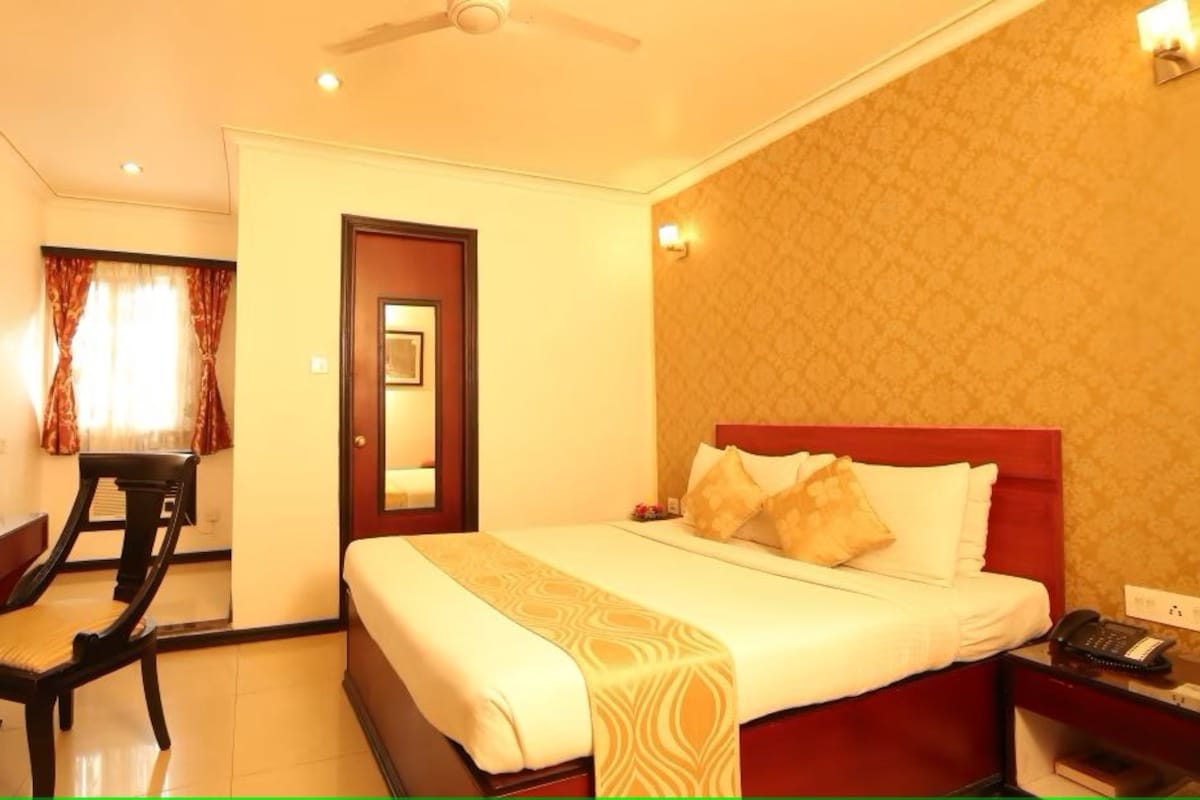 A hotel room with a bed, bedside table, chair, desk, and a mirror.