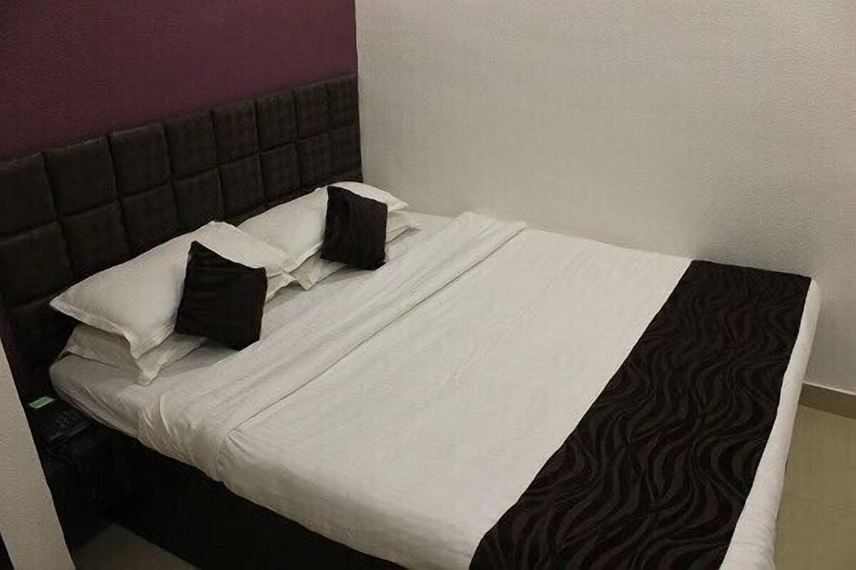 Una cama bien hecha con ropa de cama blanca y negra, un cabecero oscuro y una pared lisa de fondo.