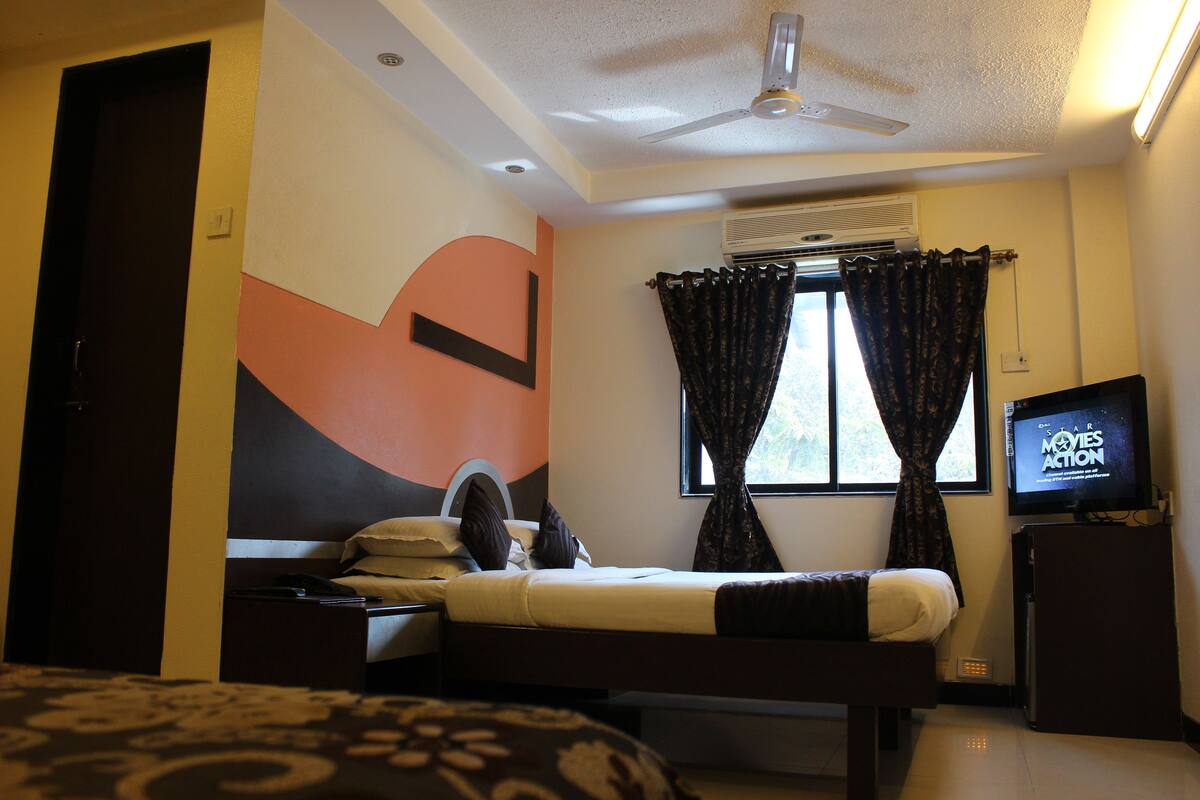 Una habitación de hotel con cama, escritorio, televisor y aire acondicionado.