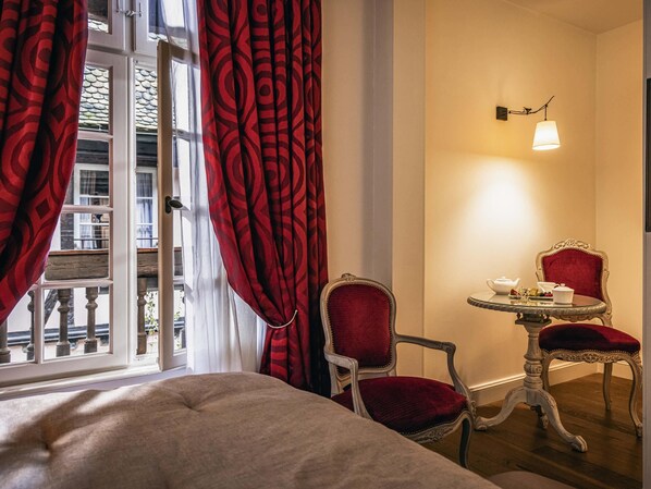 A hotel room with a bed, two red upholstered chairs, a small round table with a teapot and cups, and a wall-mounted lamp. - Cour du Corbeau Hotel Strasbourg - MGallery Collection (Strasbourg)