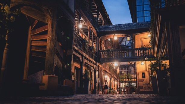 A cobblestone street with traditional European architecture, including balconies and wooden beams.