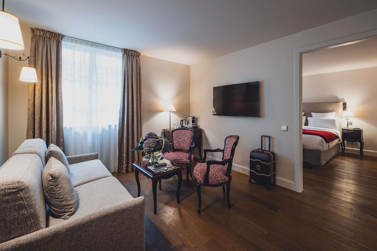 A hotel room with a sofa, chairs, a small table with a vase of flowers, a television, and a bed with a red blanket.