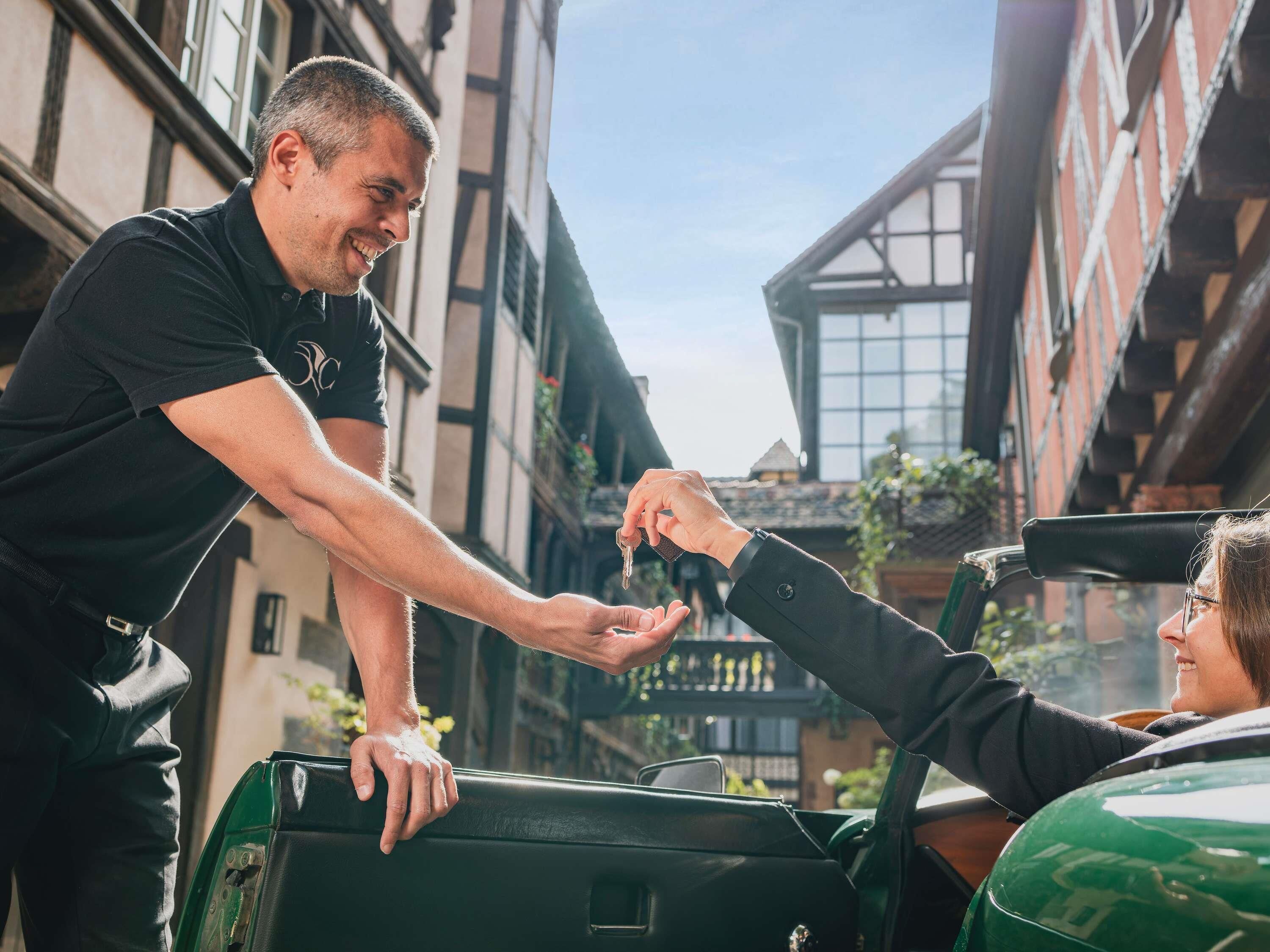 A person handing over keys to another person in a narrow street with buildings.