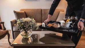 A tray with bread, a vase of flowers, and glasses of wine on a table in a room with a sofa and a chair.