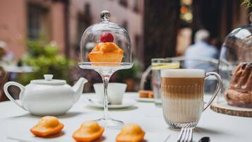 A table with a teapot, a cup of coffee, a dessert in a glass dome, and pastries.