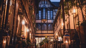 A narrow street with traditional half-timbered buildings, outdoor seating, and potted plants.