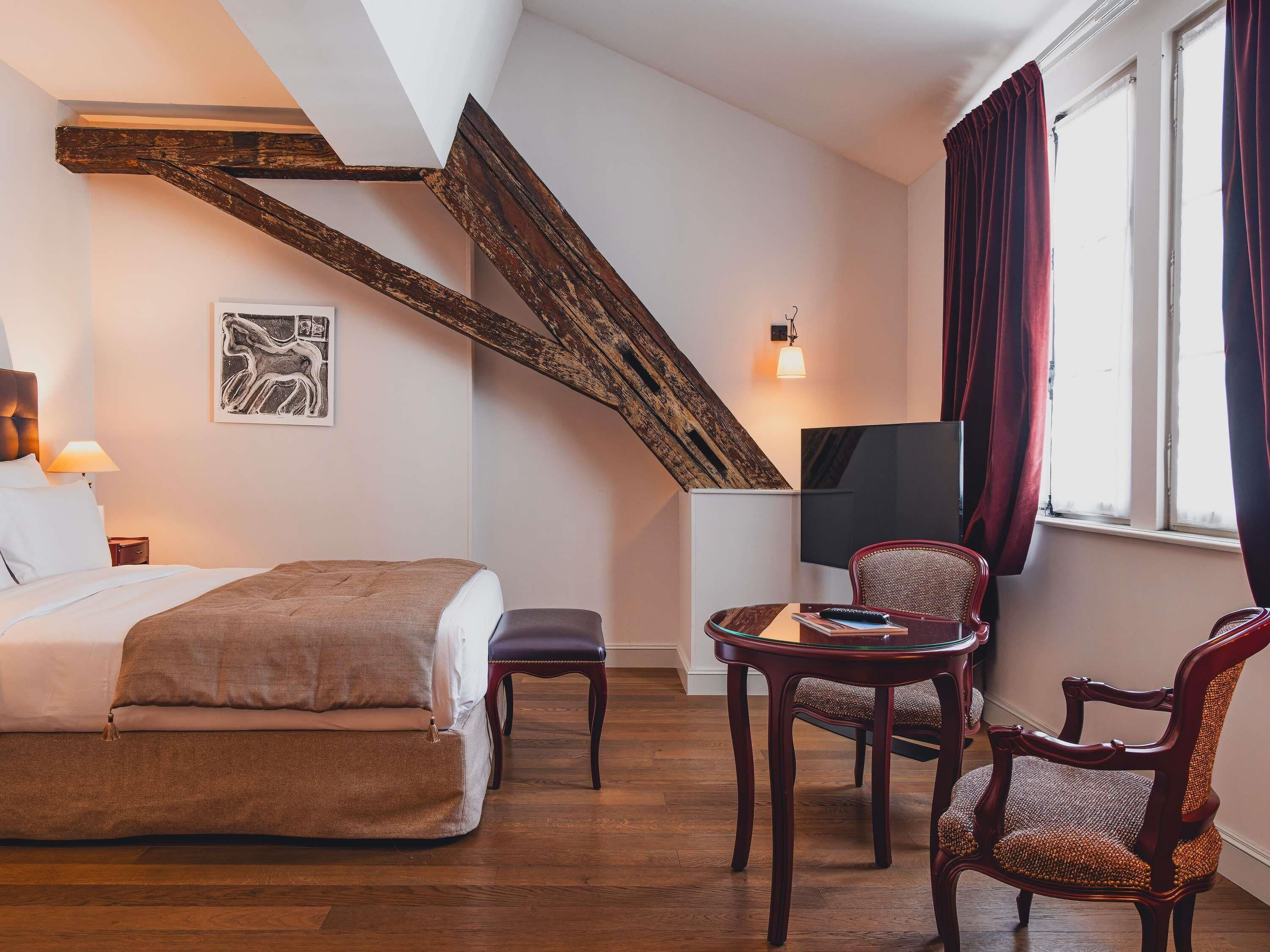 Een slaapkamer met een bed, een stoel, een klein tafeltje, een televisie en een raam met gordijnen.