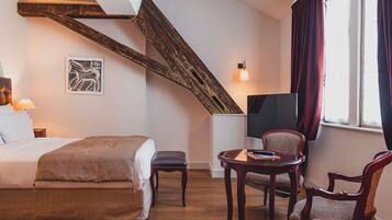 Een slaapkamer met een bed, een stoel, een klein tafeltje, een televisie en een raam met gordijnen.