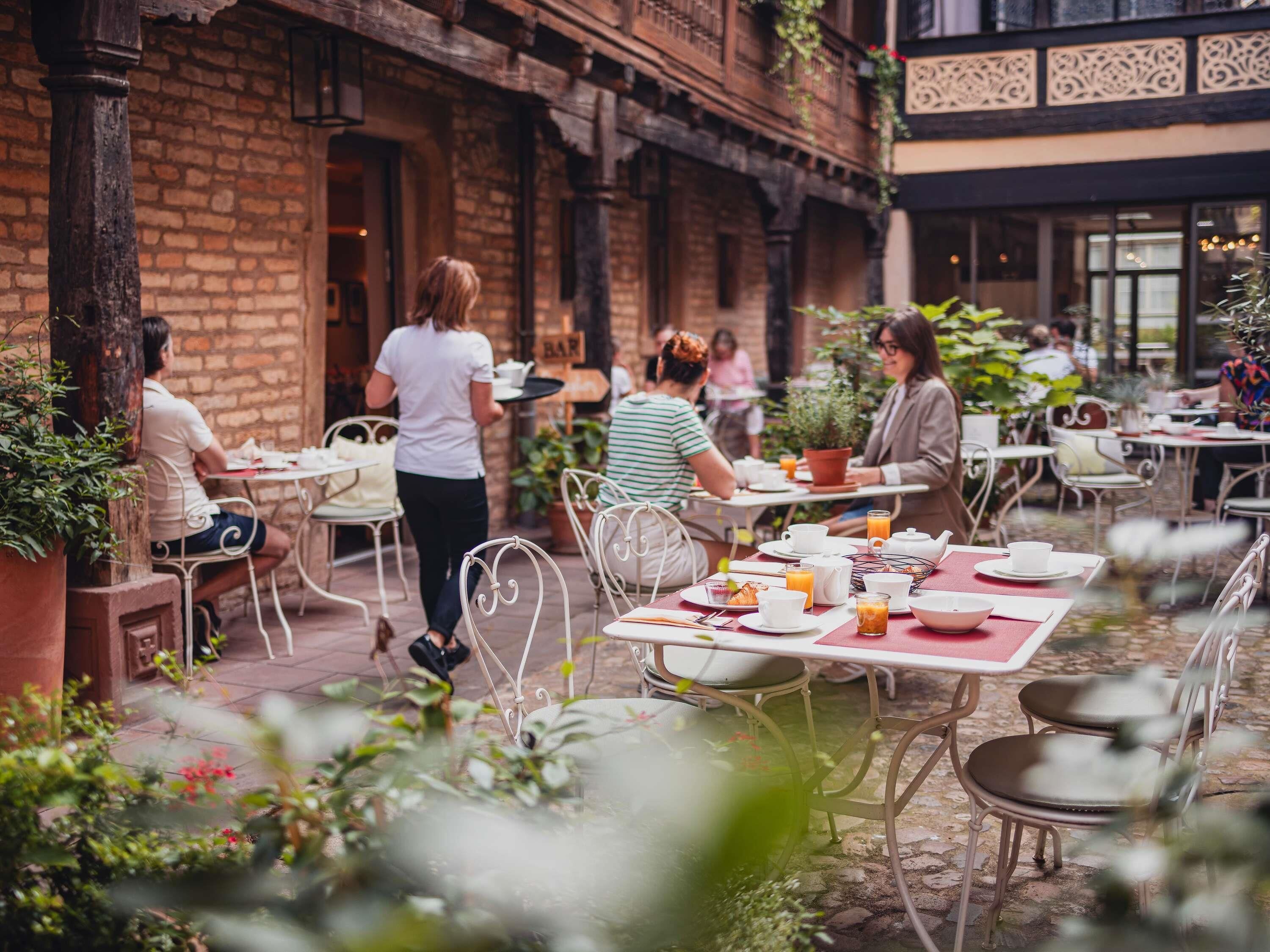 Un café en plein air avec des murs en briques, des chaises et des tables en métal, le tout aménagé pour accueillir les clients.