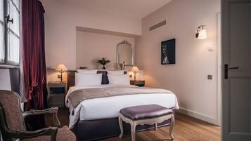 A bedroom with a large bed, bedside tables, a chair, a bench, a mirror, and a door.