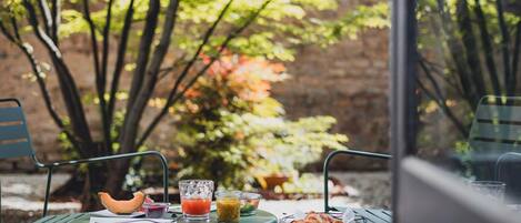 A table with a bowl of croissants, a glass of orange juice, and a glass of red juice. There are also some fruits and a notebook on the table.