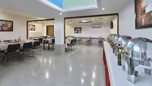 A spacious dining area with multiple tables and chairs, a long buffet line with food dispensers, and a skylight ceiling. - Regale Inn (New Delhi)