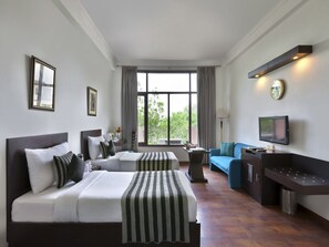 Ein Hotelzimmer mit zwei Betten, einem Schlafsofa, einem Fernseher und einem großen Fenster mit Vorhängen.