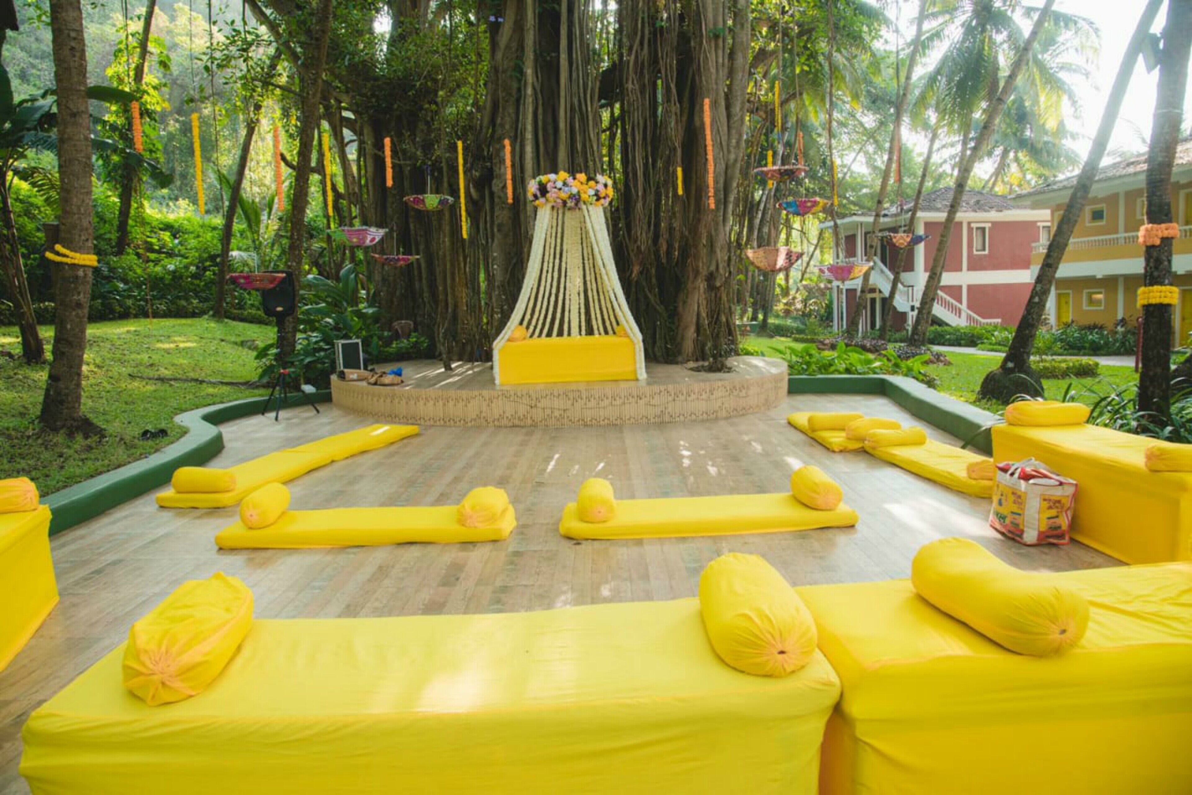 A circular seating area with yellow cushions and a central decorative piece, surrounded by lush greenery and trees.