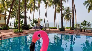 Ein Pool mit einem Flamingo-Schwimmtier, umgeben von Palmen und Liegestühlen.
