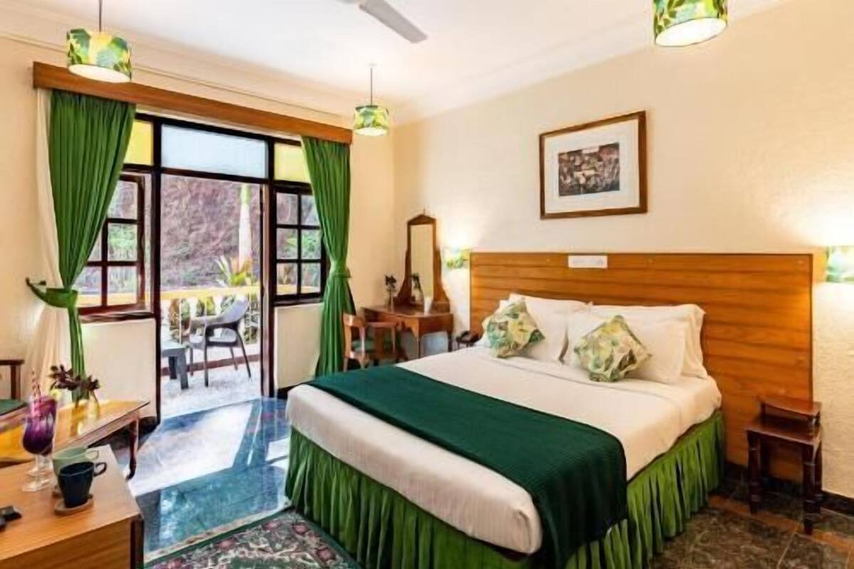 A hotel room with a bed, a desk, a chair, a window with curtains, and a view of the outdoors.