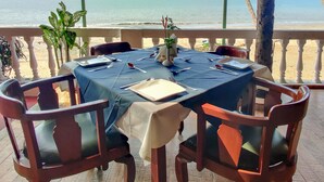 Mesa lista para comer con vista al mar, bajo una zona con techo rojo y sillas de madera.