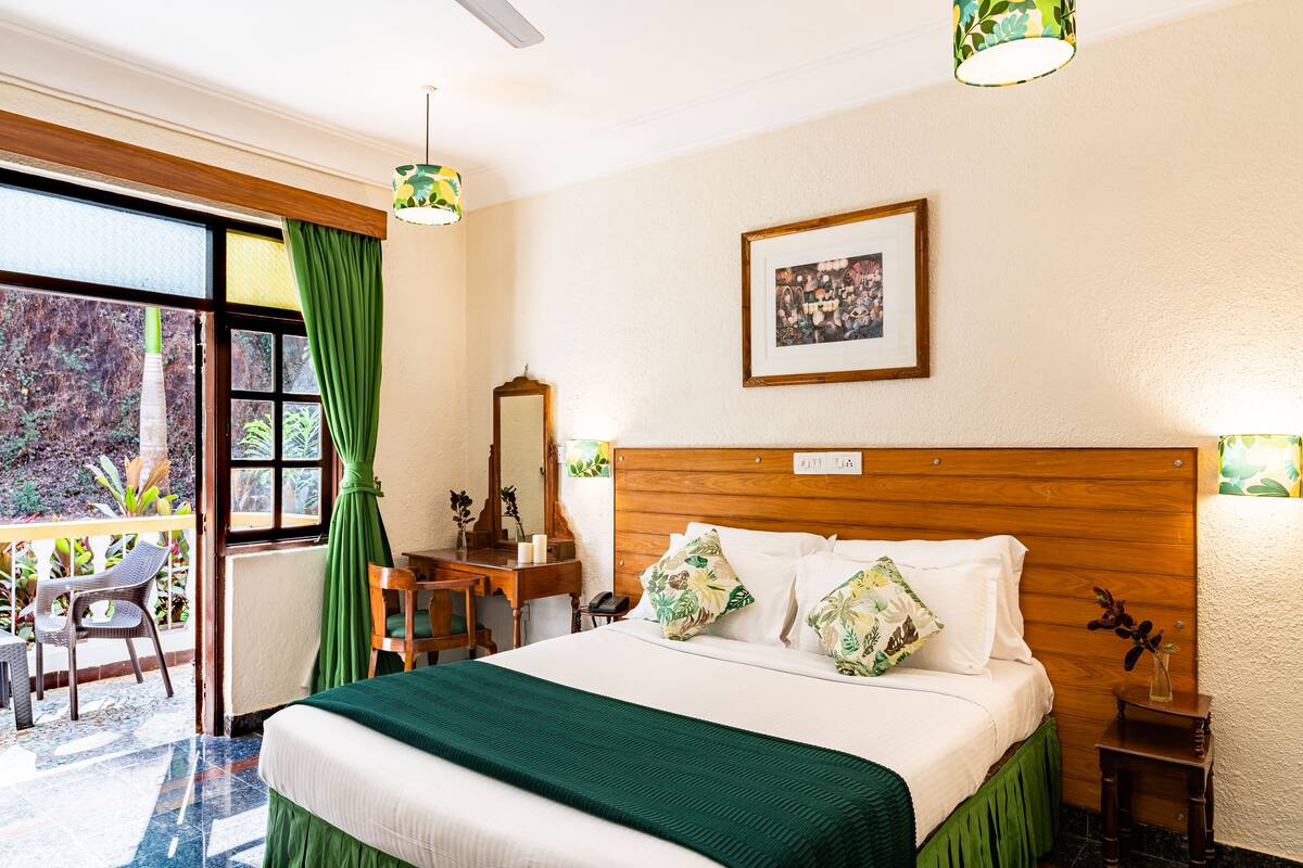 A hotel room with a bed, a desk, a chair, a mirror, and a view of the outdoors.