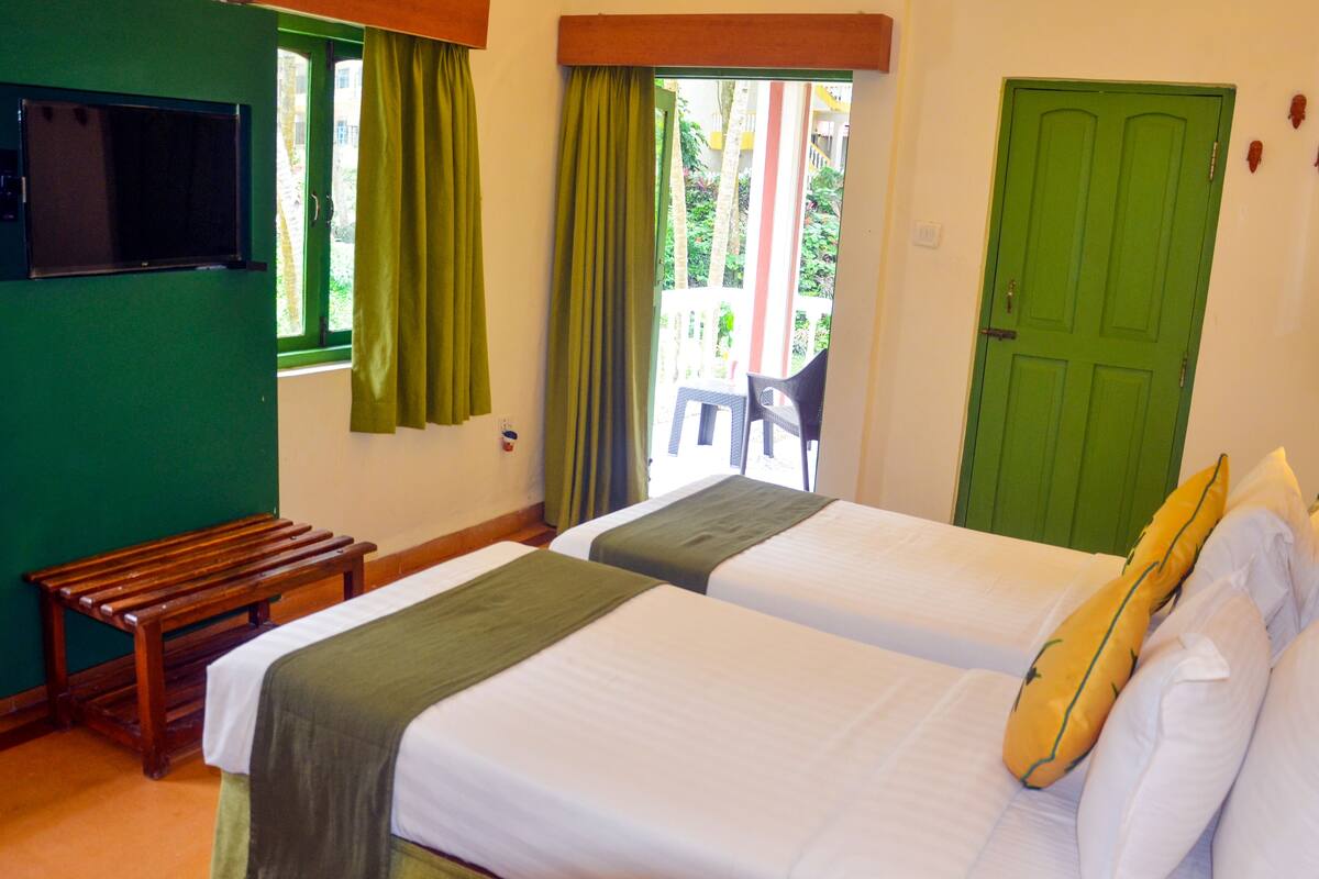 A room with two beds, a bench, a TV, and a green door.