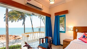 Una habitación con balcón que da a la playa, una cama con cabecera de madera y una mesa con un florero.
