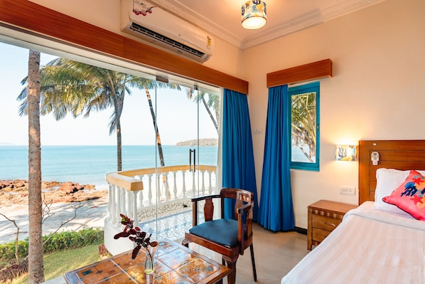 A room with a balcony overlooking a beach, a bed with a wooden headboard, and a table with a vase.
