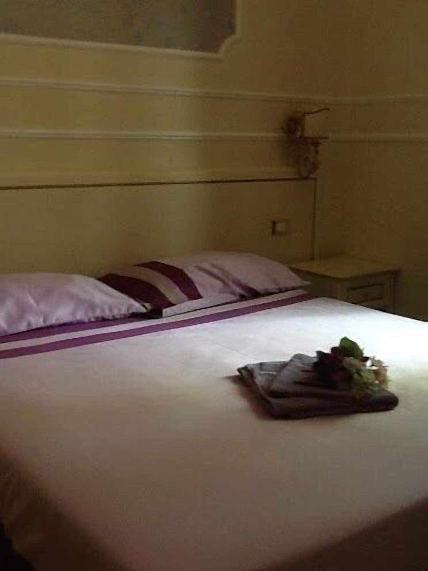 A neatly made bed with a white and purple striped bedspread, a small bedside table with a lamp, and a wall-mounted decoration.