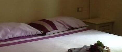 A neatly made bed with a white and purple striped bedspread, a small bedside table with a lamp, and a wall-mounted decoration.