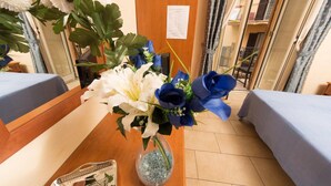 A hotel reception area with a wooden desk, a vase of flowers, and a bulletin board with a menu. - Fitzroy Allegria Suites (Rome)