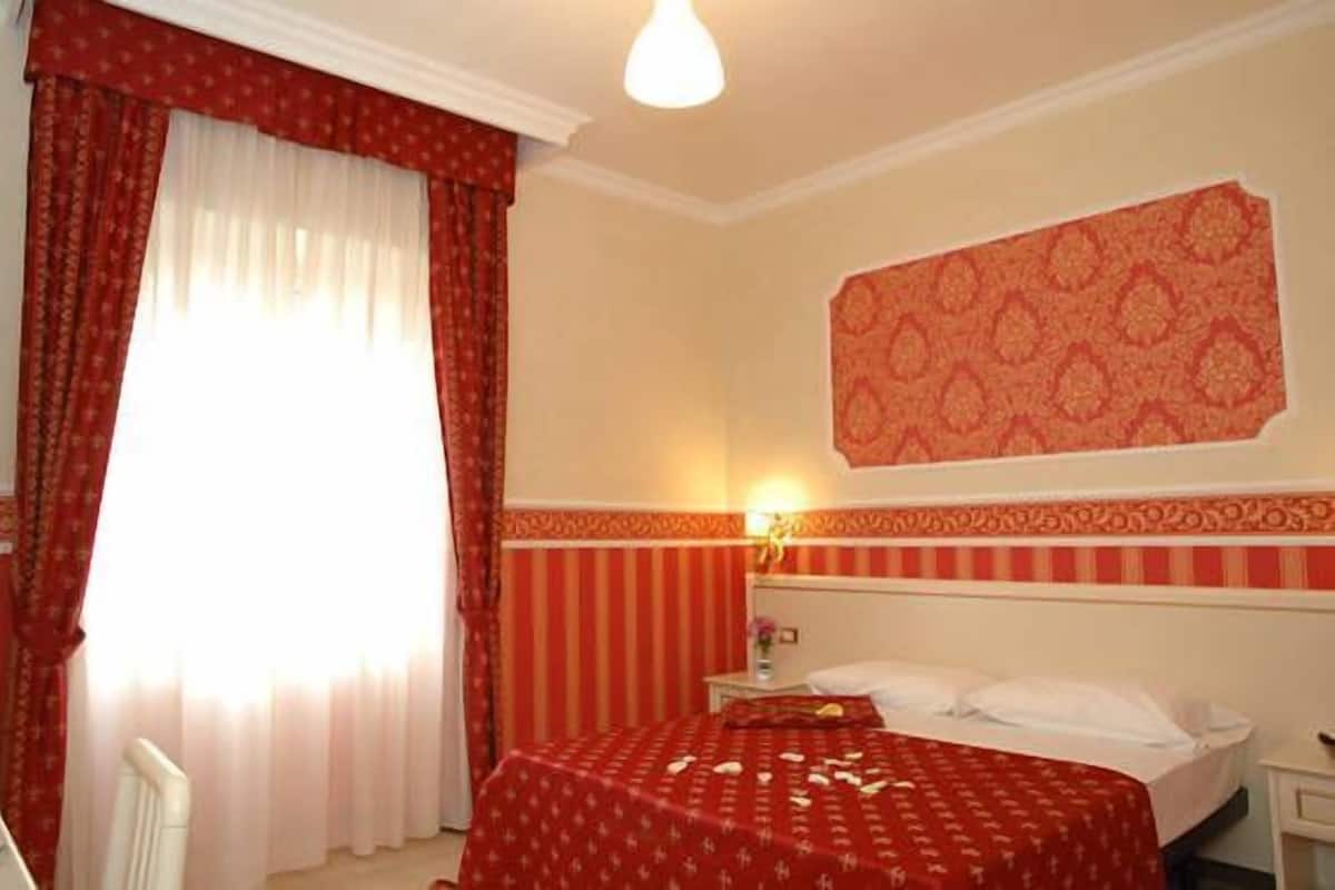 A hotel room with a bed, a nightstand, a lamp, and a window with curtains.