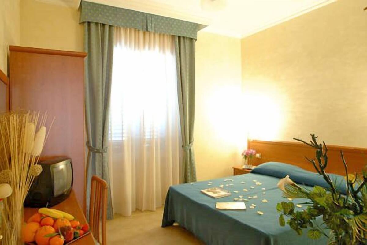 A hotel room with a bed, a desk with a television, and a window with curtains.