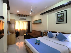 A hotel room with a bed, a desk, a chair, a sofa, a ceiling fan, an air conditioning unit, and a framed picture on the wall. - Ontime Hotel (Mumbai)
