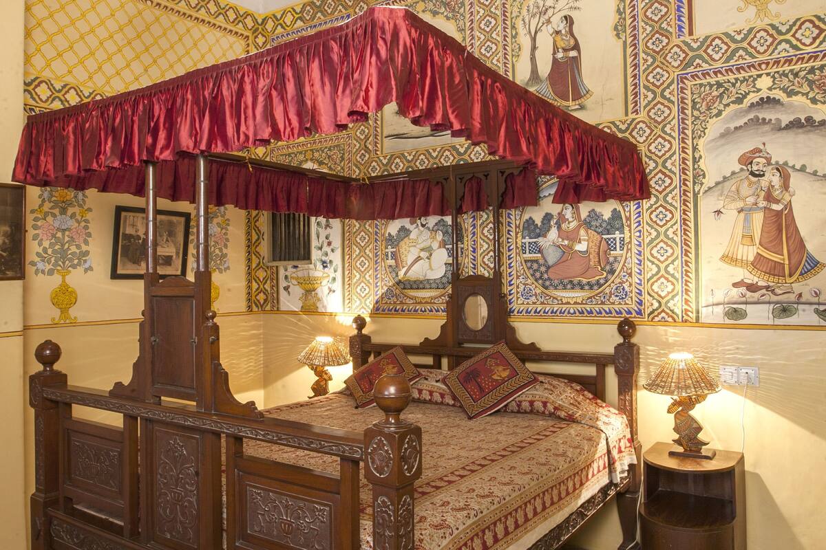 A traditional bed with a canopy, ornate wall decorations, and patterned floor tiles.