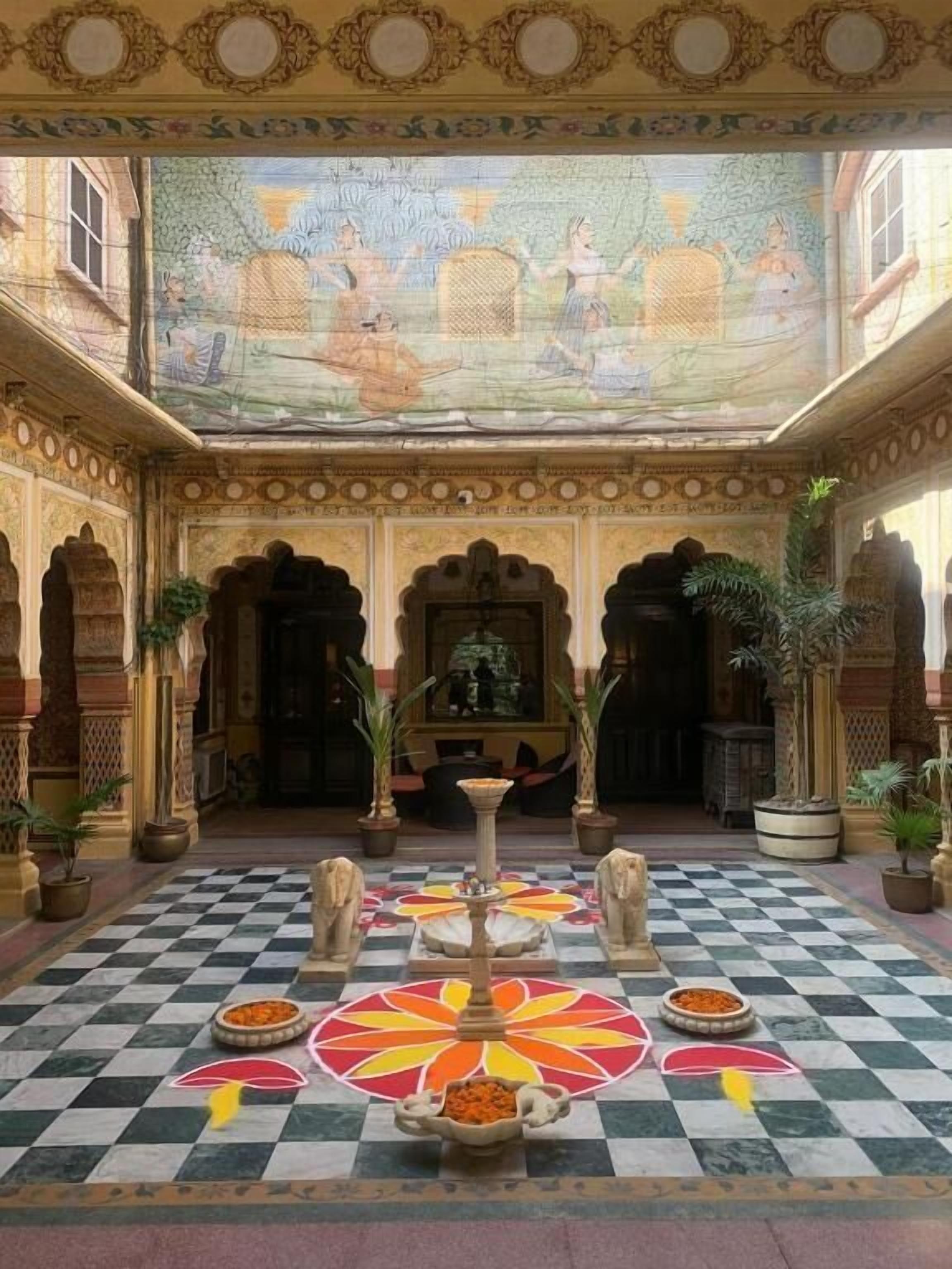 Une cour somptueuse, dotée d’un sol à carreaux, de piliers décoratifs et d’une fontaine centrale.