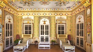 A room with ornate yellow and white patterned walls, a central arched doorway, and a seating area with white furniture. - Bissau Palace (Jaipur)