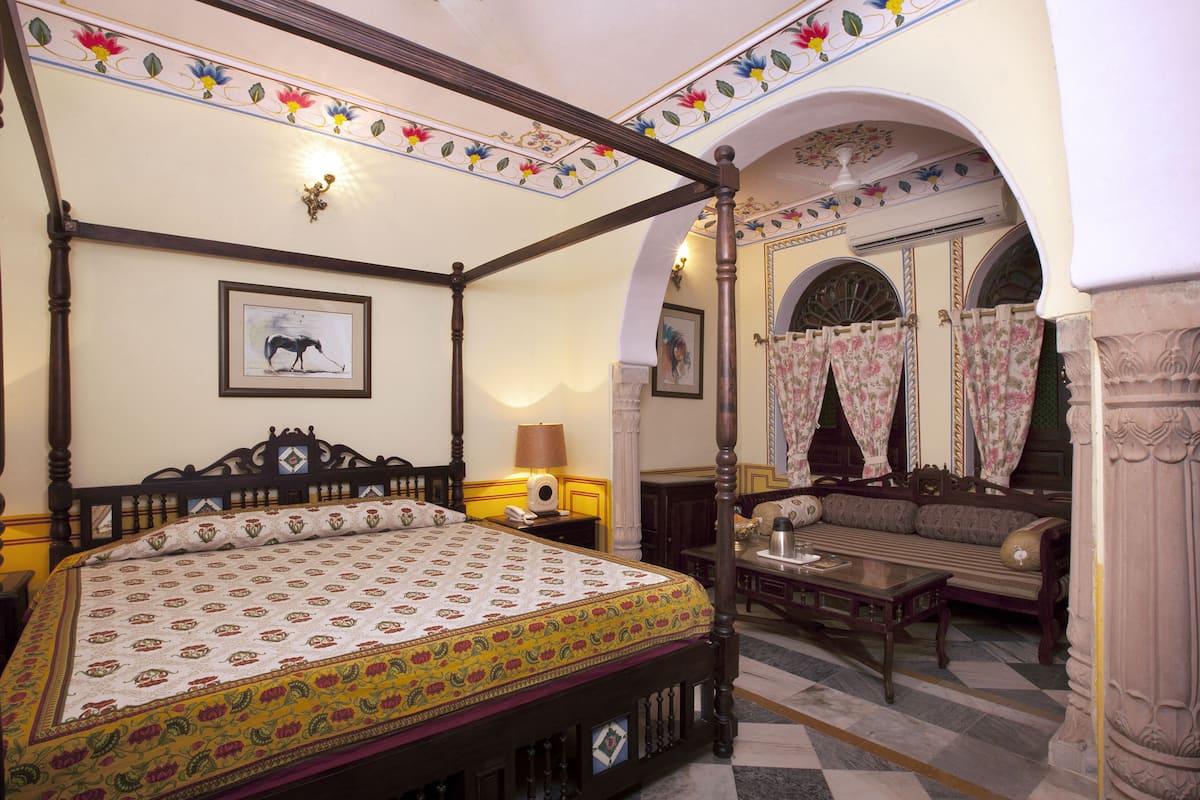 A four-poster bed with a patterned bedspread, a bedside table with a lamp, and a framed picture on the wall.