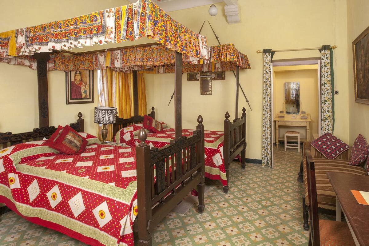 A traditional four-poster bed with a quilt, a wooden desk, and a mirror.