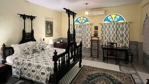 A bedroom with a four-poster bed, a small table, a chair, and a decorative rug. - Bissau Palace (Jaipur)