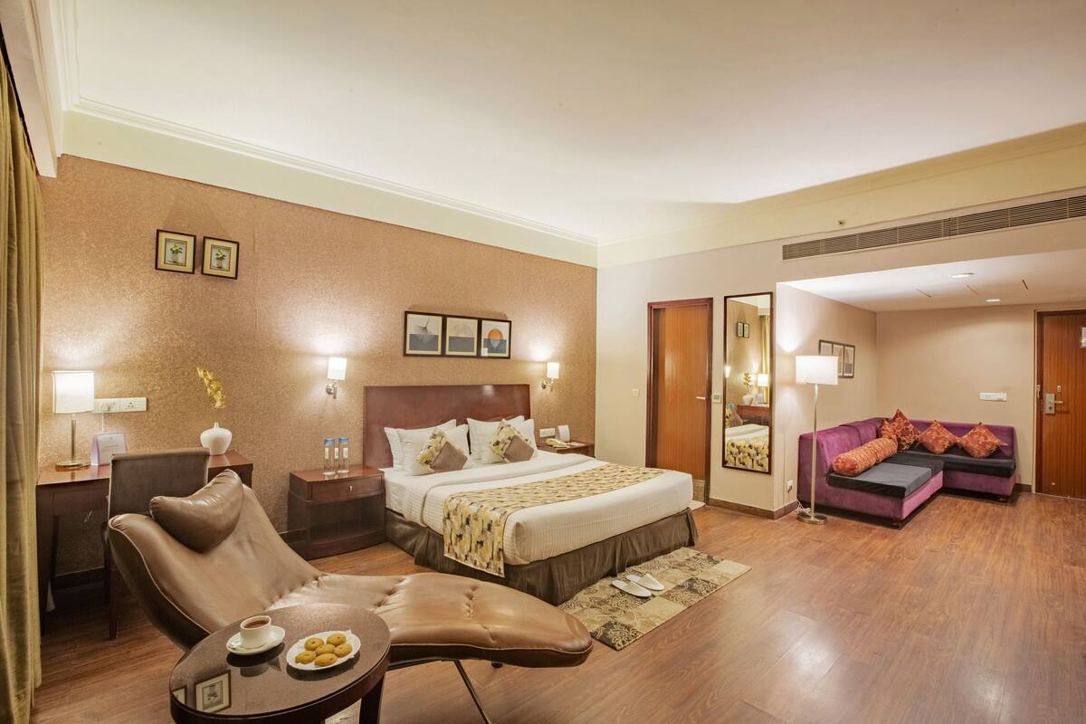 Une chambre d’hôtel avec un lit, un canapé, une chaise, une table avec une assiette de nourriture et un miroir.