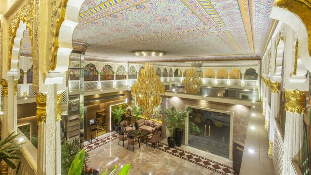 Un lobby lujoso con diseños ornamentales en el techo, una zona de estar con sofás y sillones, y una imponente escalera.