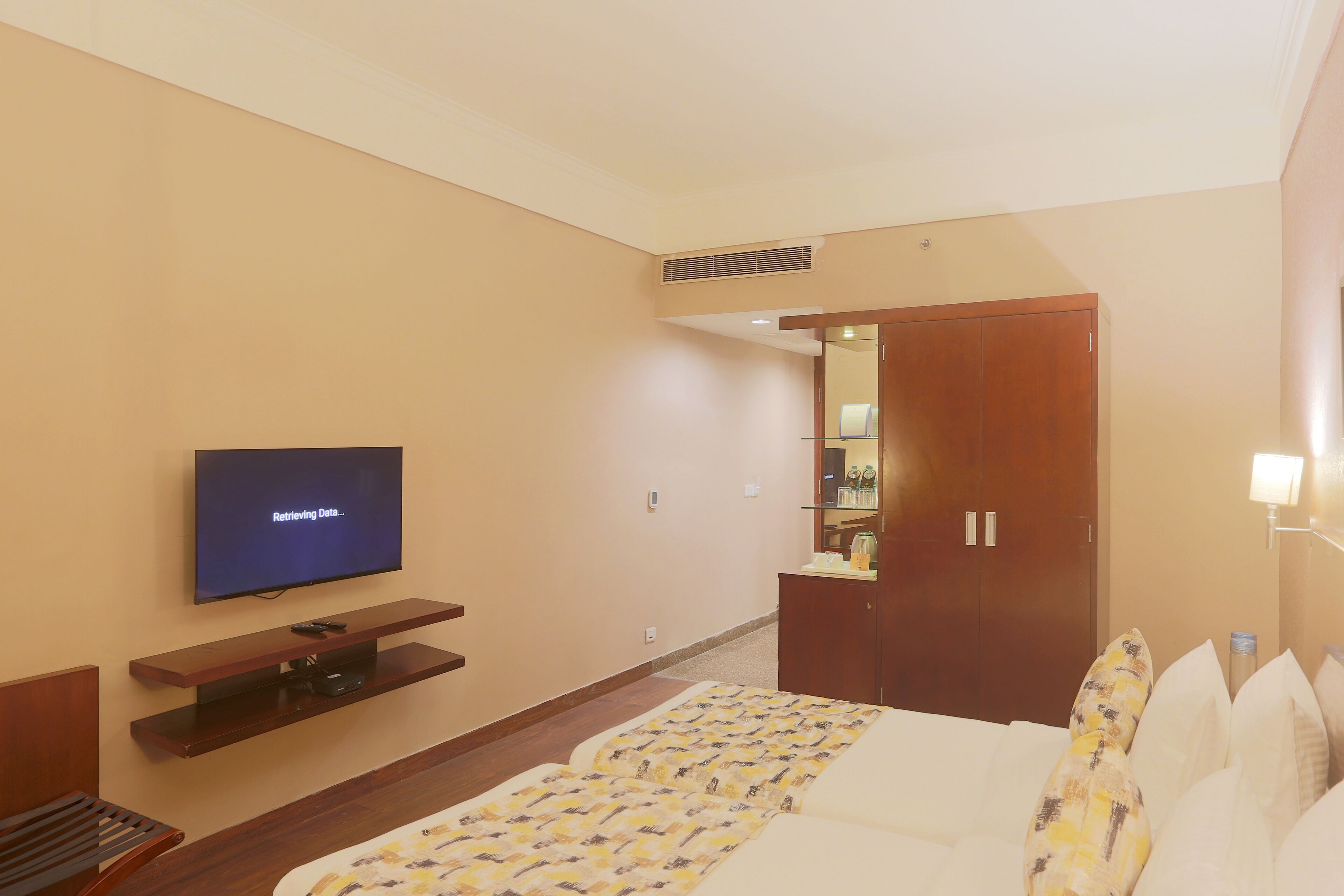 A hotel room with a bed, a TV on a stand, a wardrobe, and a small desk with a mirror.