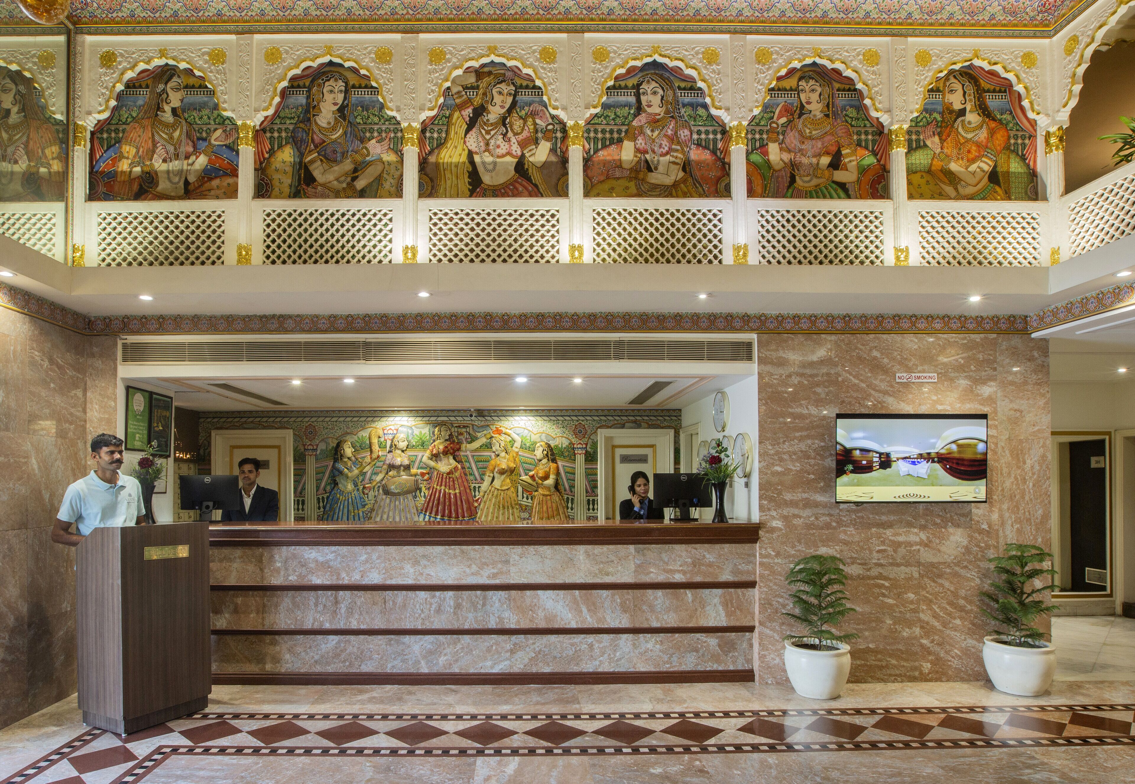 A hotel lobby with a reception desk, a man at the podium, and a mural of women.