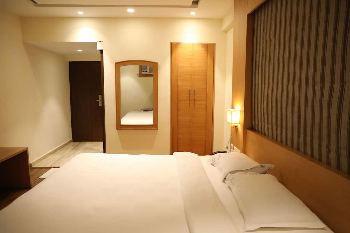 Una habitación de hotel con una cama grande, un armario de madera, un espejo y una cortina a rayas.
